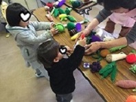 編みぐるみで野菜や果物の名前あてをしている子供の様子