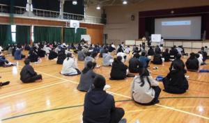 体育館で報告を聞く生徒たちの写真